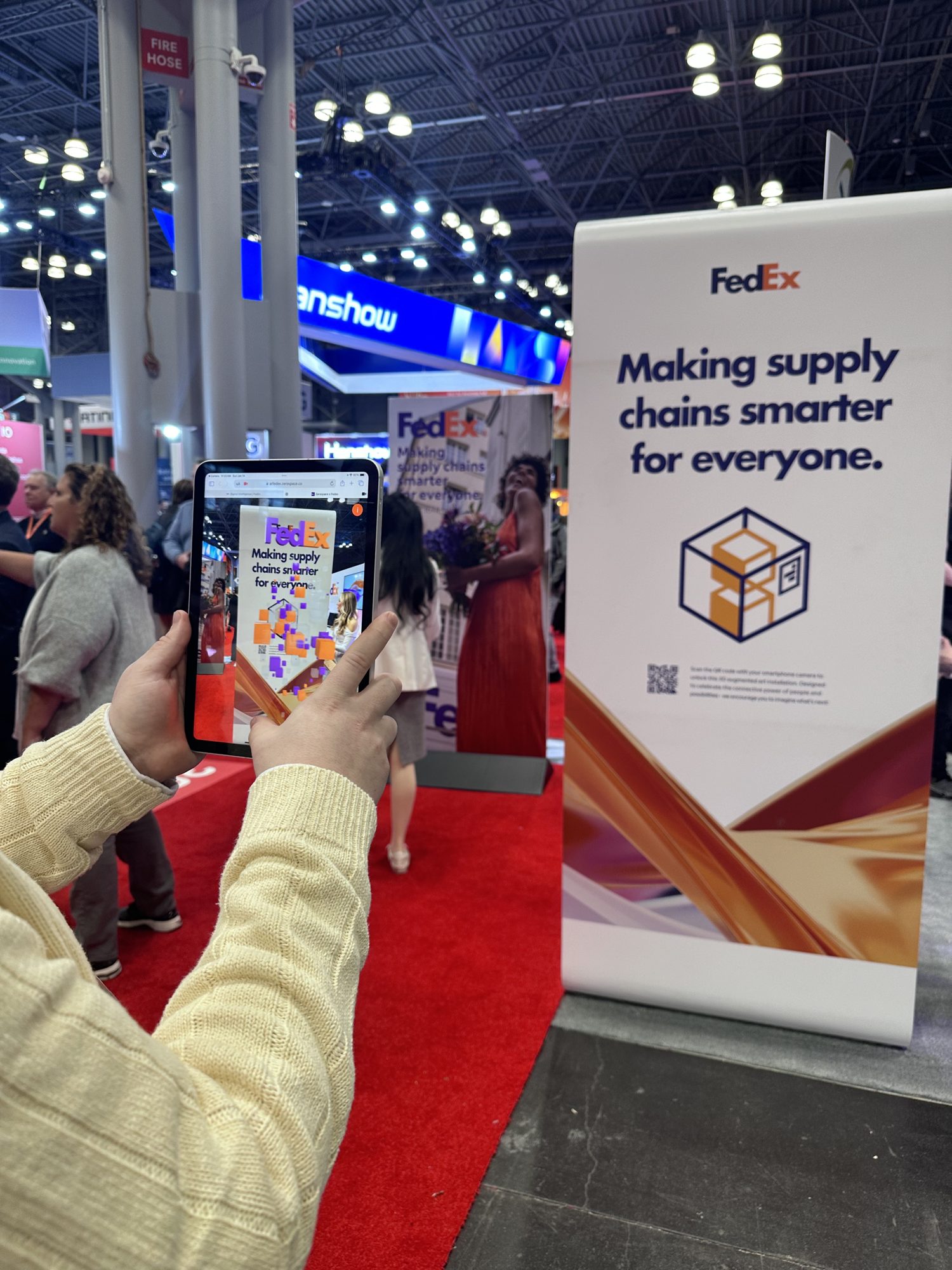 A visitor holds up a phone with the FedEx AR experience beside the Making supply chains smarter for everyone sign