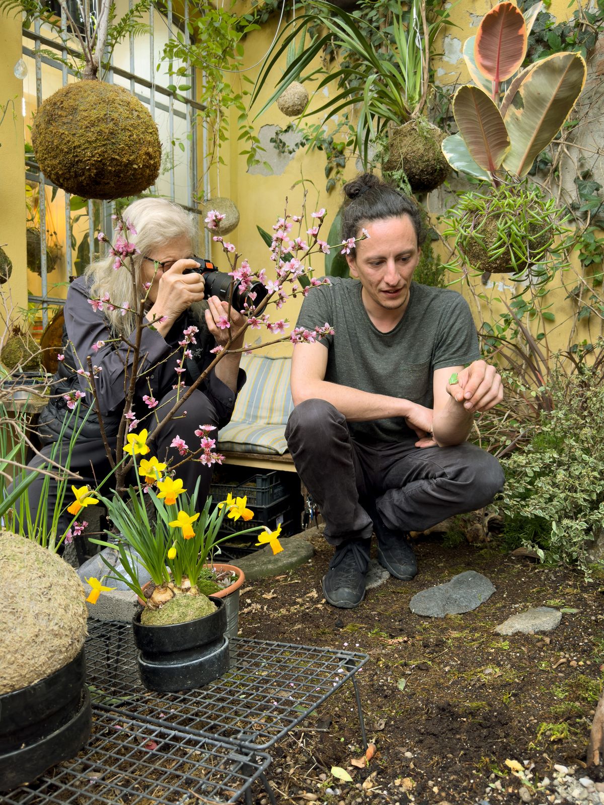 Annie Leibovitz photographs among potted plants and spring flowers in a garden as the homeowner crouches beside her