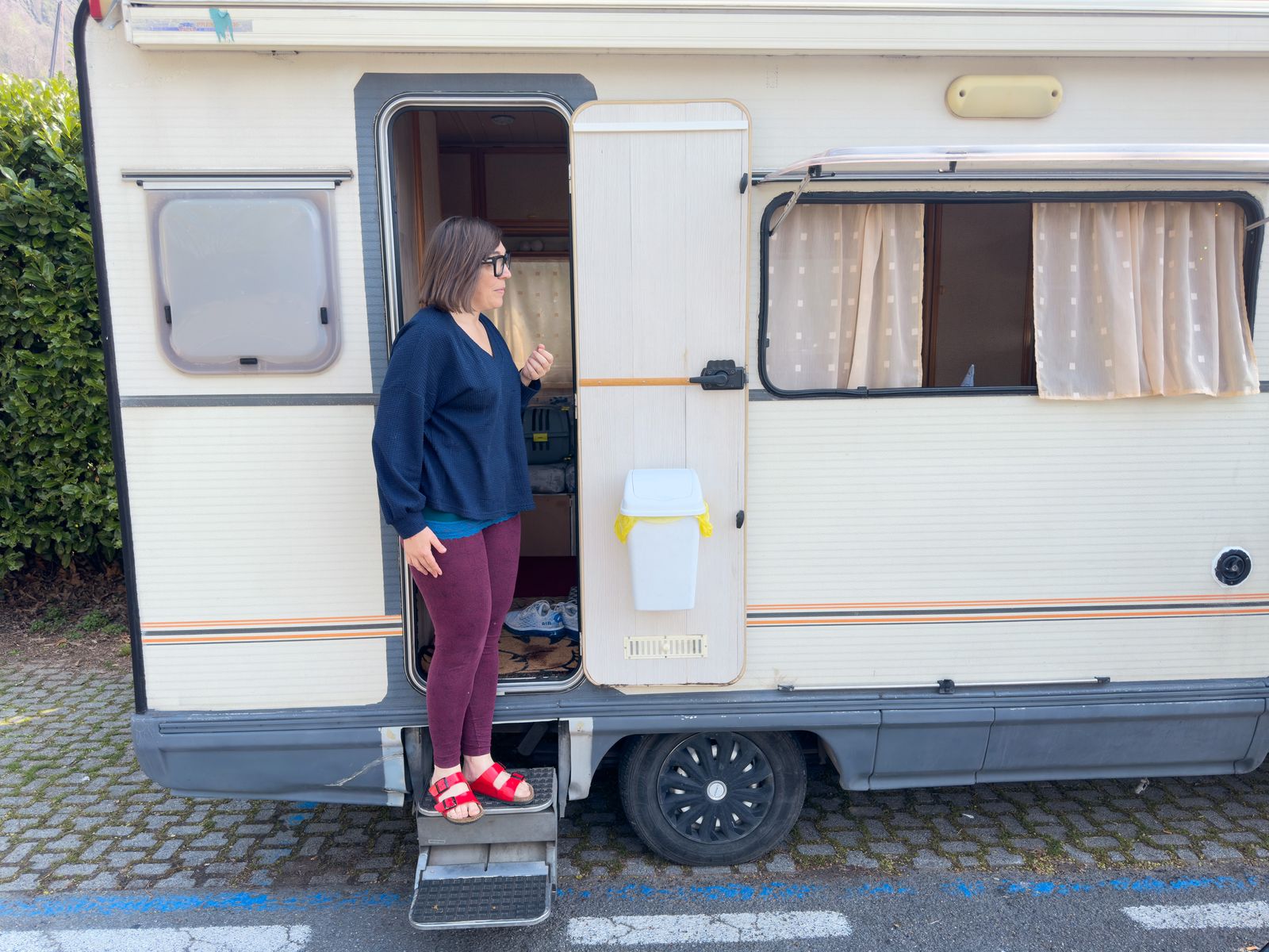 A woman stands in the doorway of her camper van home parked on a city street