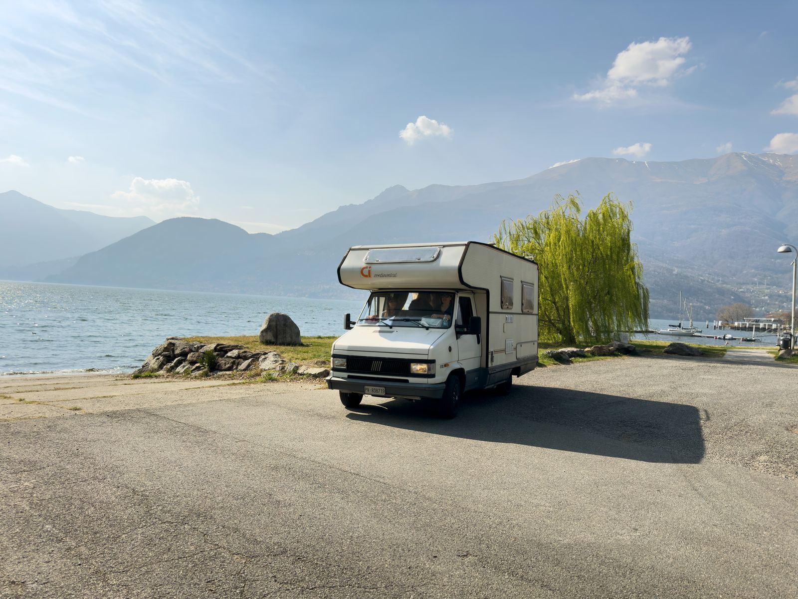 A camper van home parked on a lakeside promenade beneath mountains