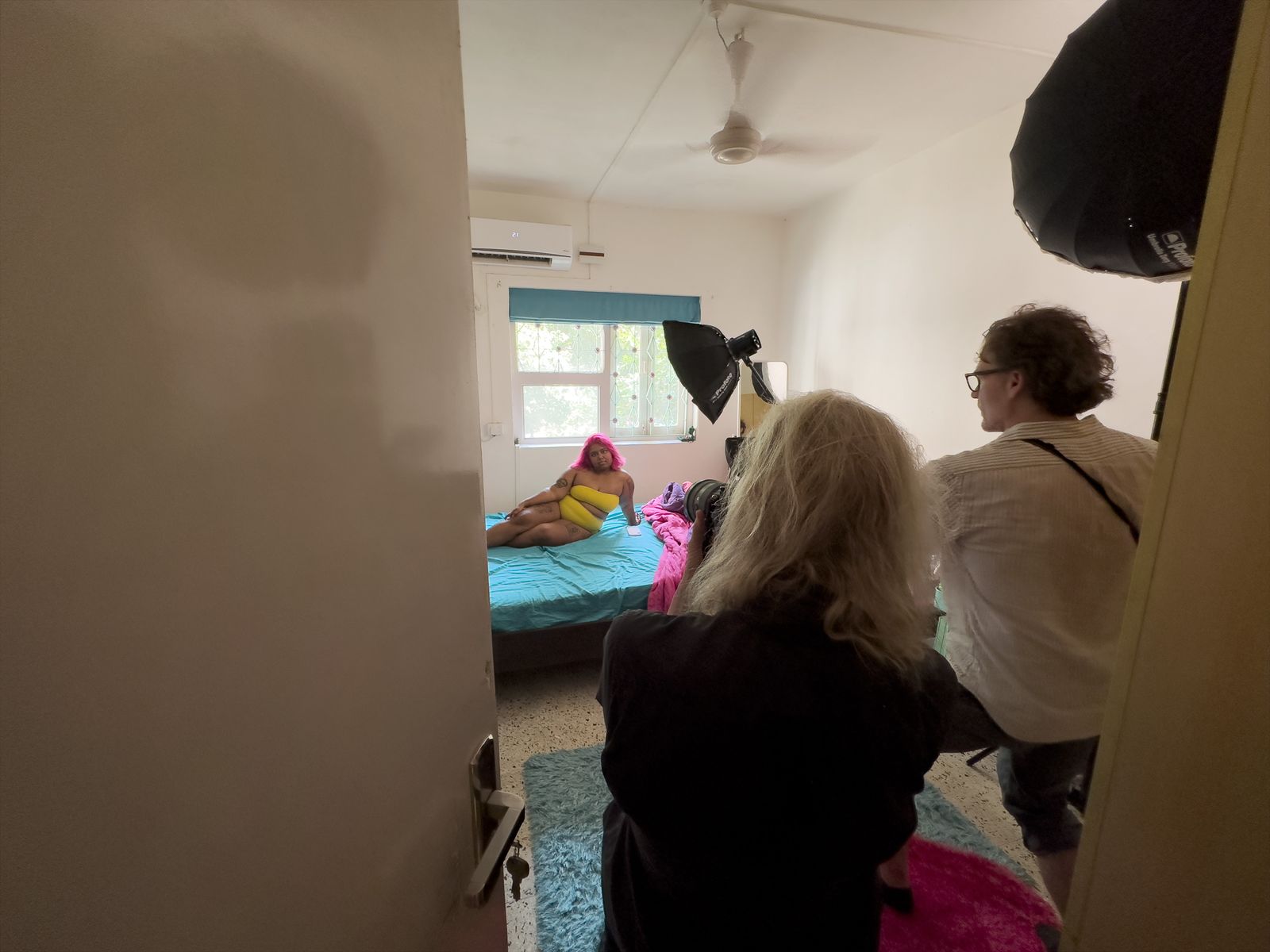 Annie Leibovitz and crew frame a bedroom portrait through a doorway, a softbox light set up beside them