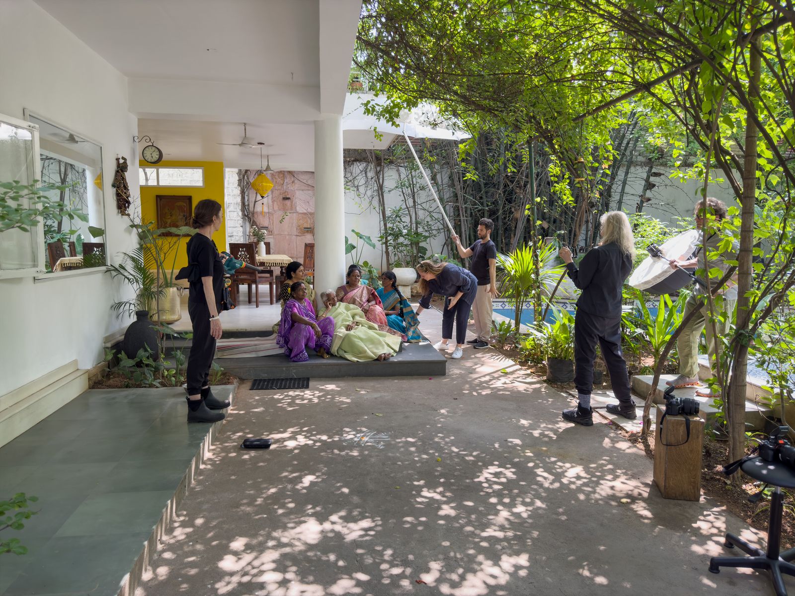 The crew sets up lights on a shaded veranda as a family gathers for their portrait in India