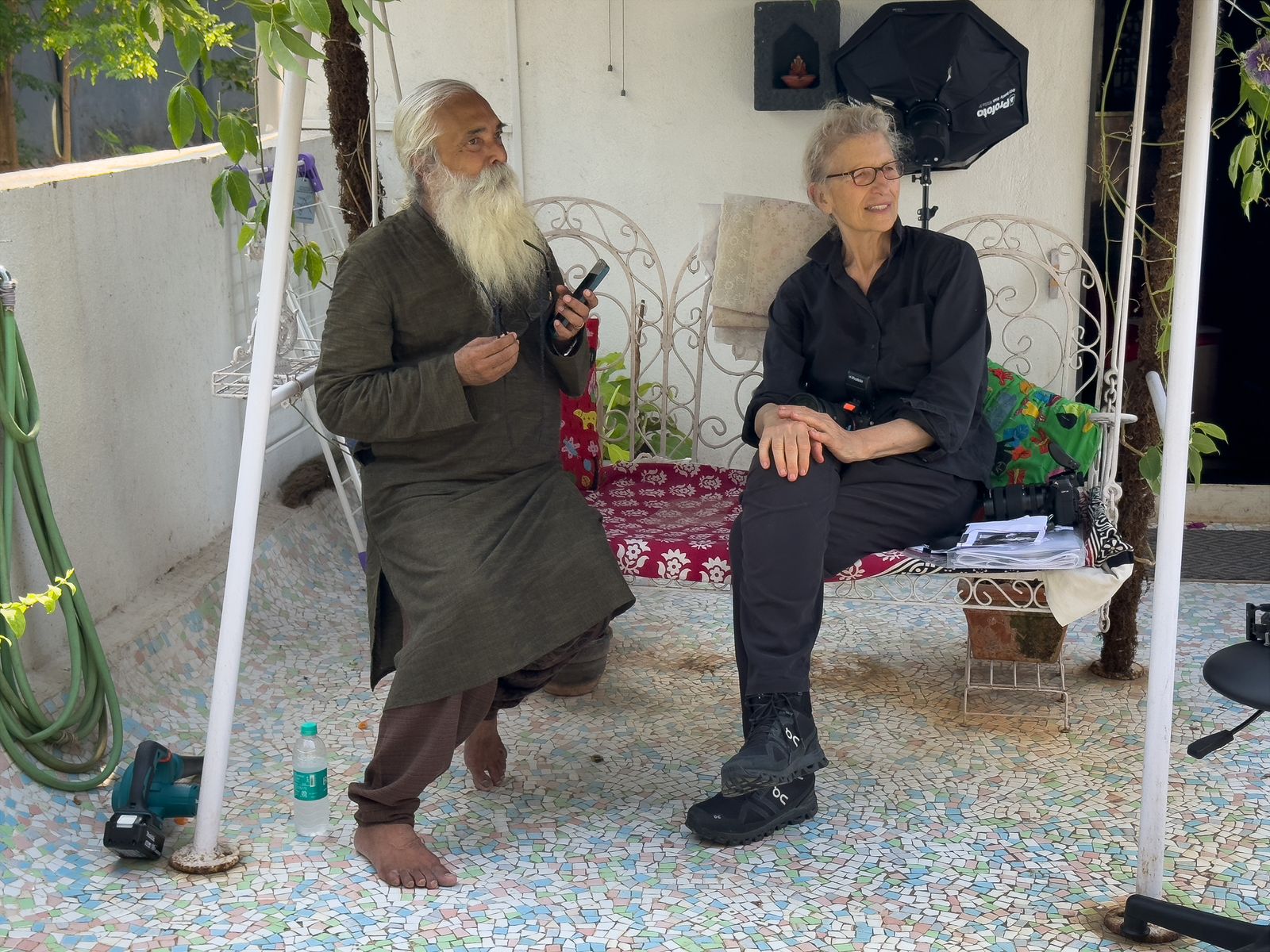 Annie Leibovitz sits with an elder on a garden swing beside a softbox between setups in India