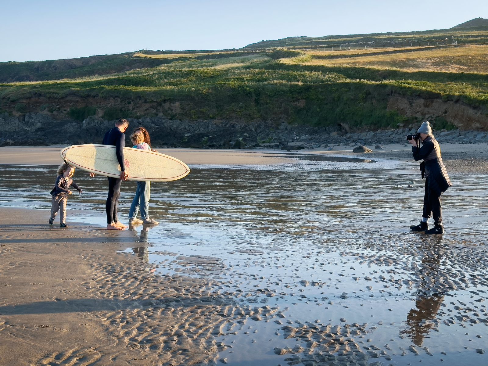 Annie Leibovitz photographs a family carrying a surfboard across the sand at low tide on a UK beach
