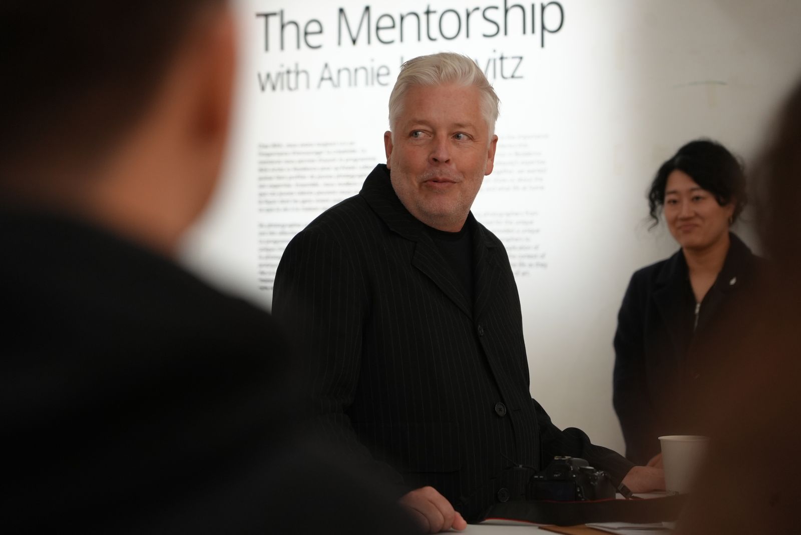 A speaker addresses guests in front of The Mentorship with Annie Leibovitz wall in Paris
