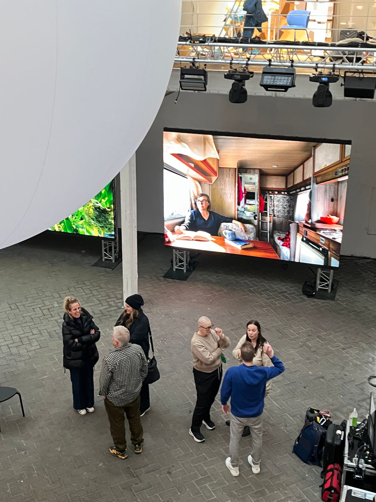 Overhead view of visitors beneath a large screen showing a Life at Home portrait in the warehouse venue