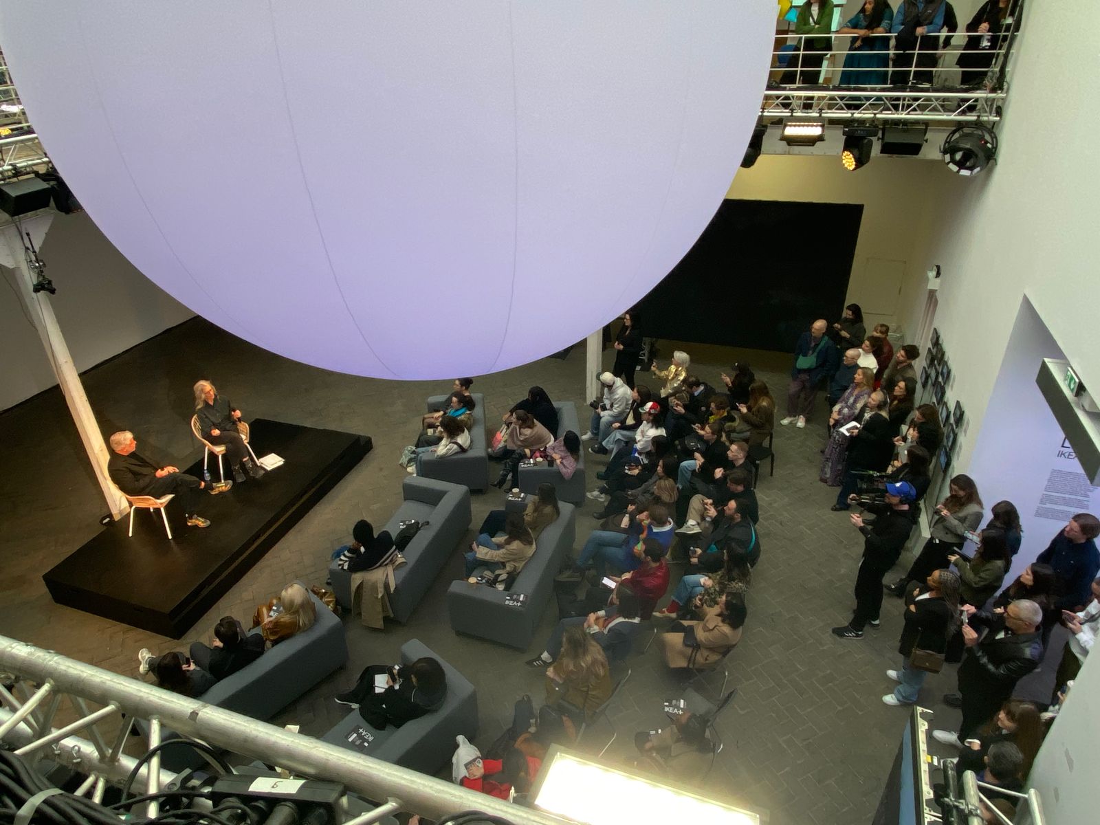 Overhead view of an audience at a talk on a low stage beneath a giant glowing balloon