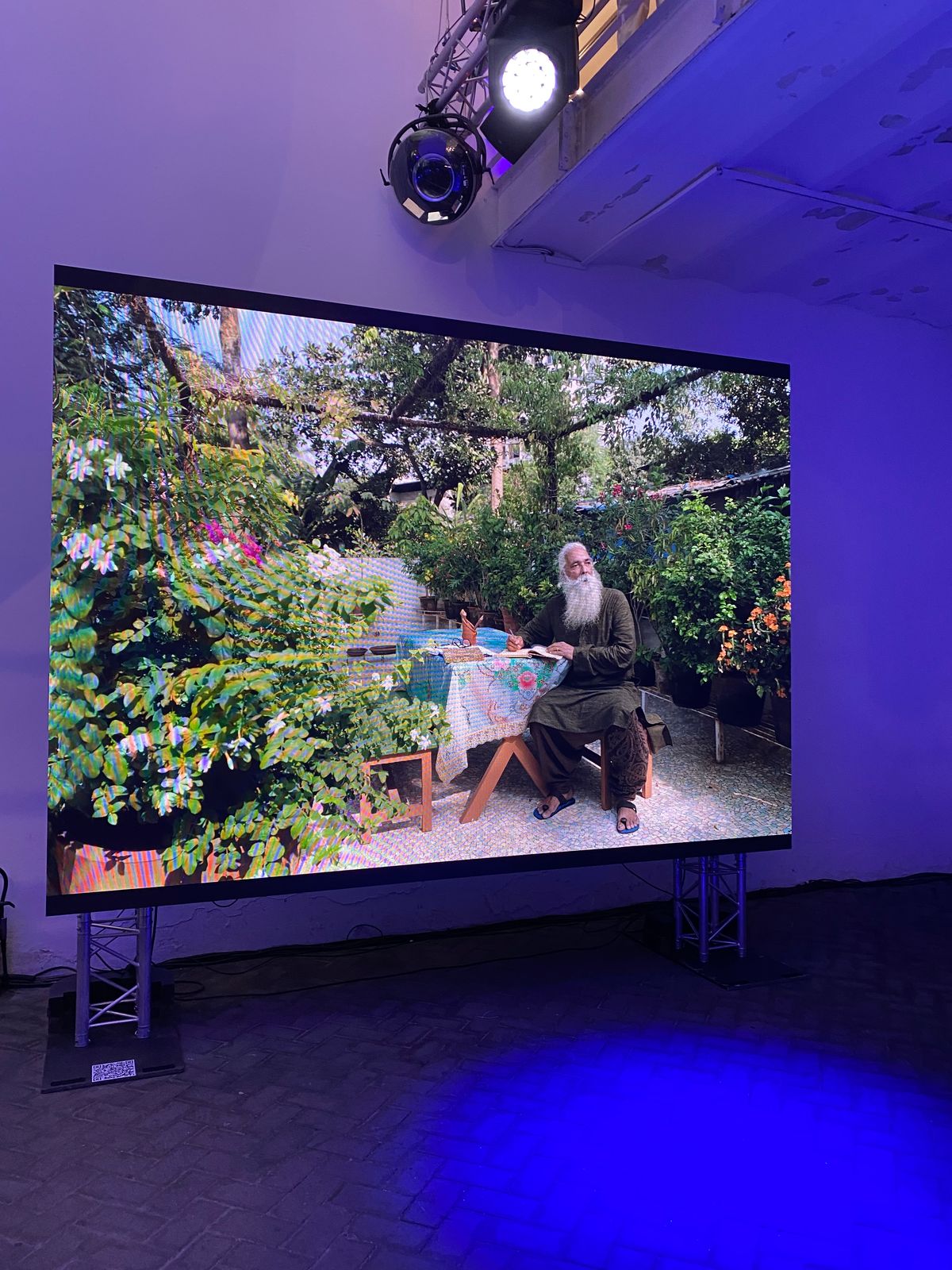 A Life at Home portrait of an elder in a flowering garden shown on a large screen under a stage light