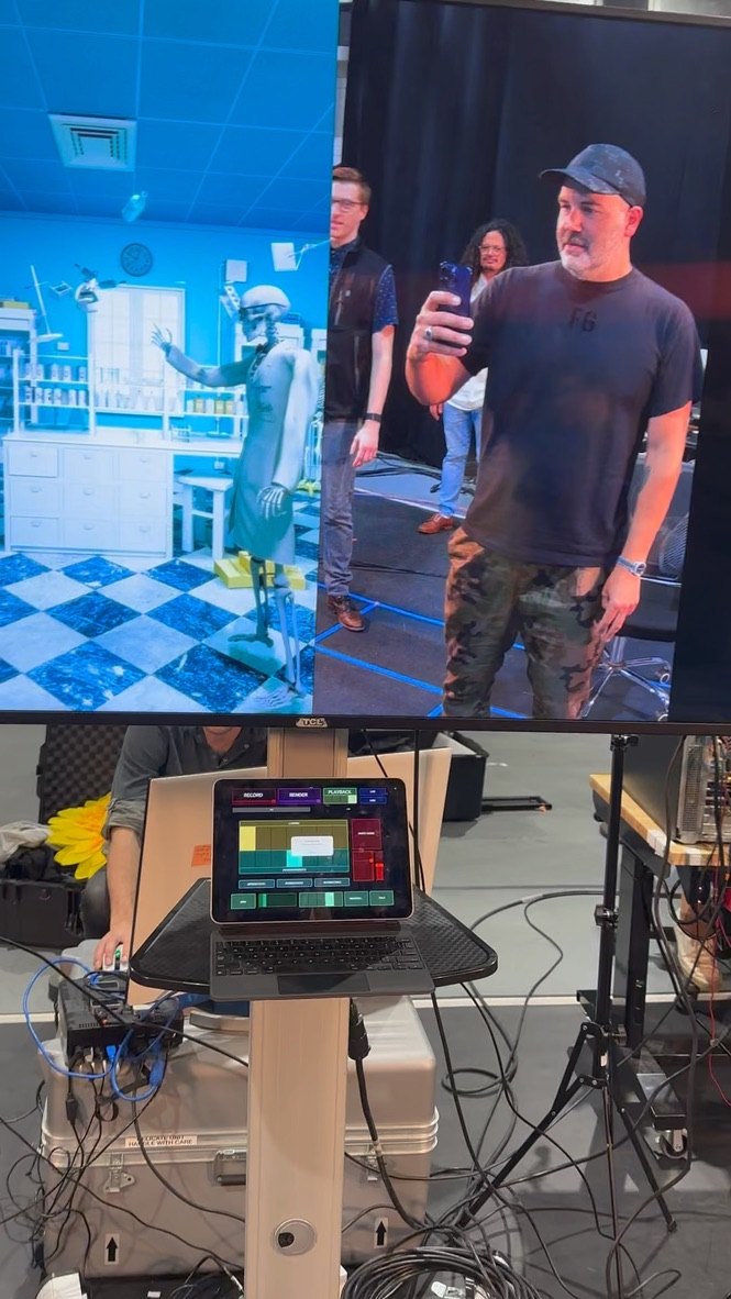 A monitor shows Bones in the lab beside the live camera feed while a crew member films