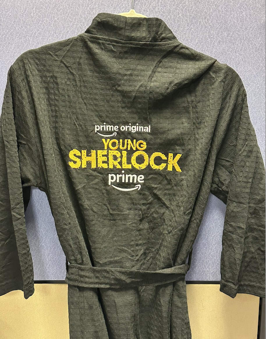 A custom olive Young Sherlock robe with the series logo embroidered in yellow