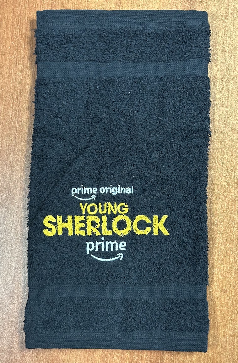 A navy hand towel embroidered with the Young Sherlock logo